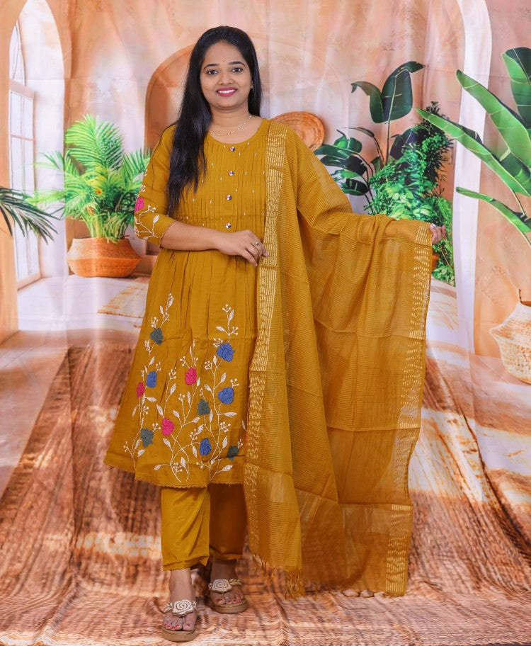 Woman in a mustard yellow traditional outfit with floral embroidery indoors.