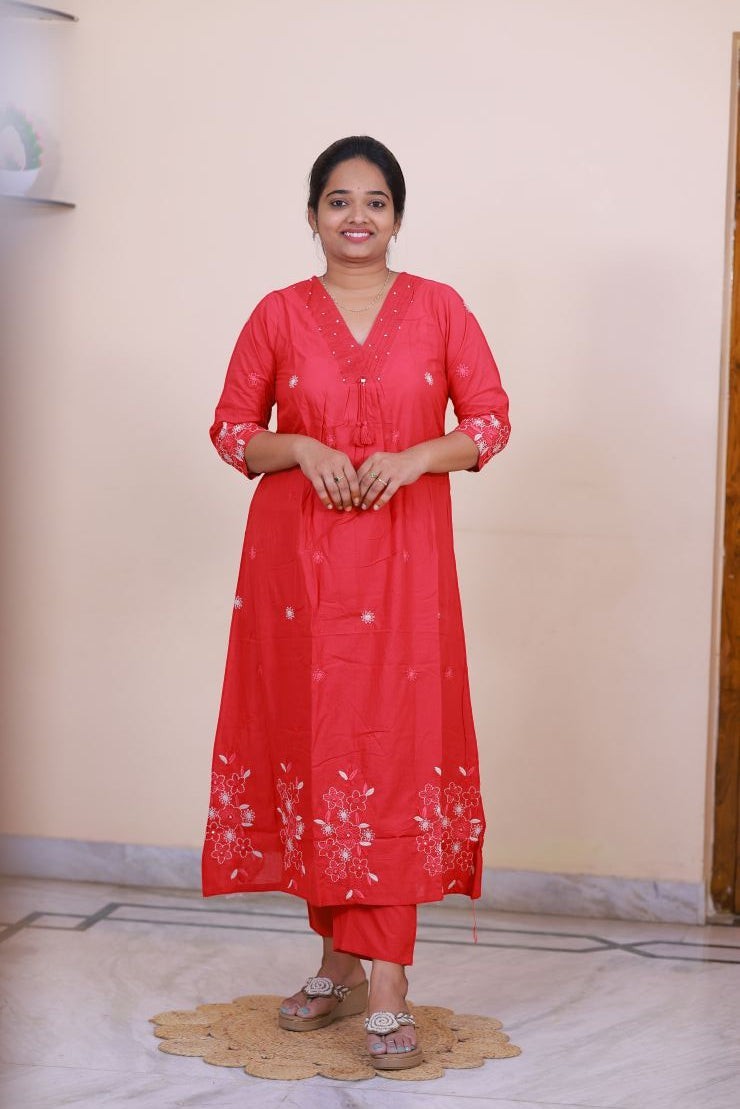A woman wearing a SreeVastra red cotton 3-piece dress with white floral embroidery and a V-neckline.