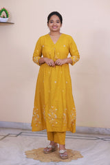 A woman wearing a mustard yellow SreeVastra cotton 3 piece dress with white floral embroidery and tassel detail.