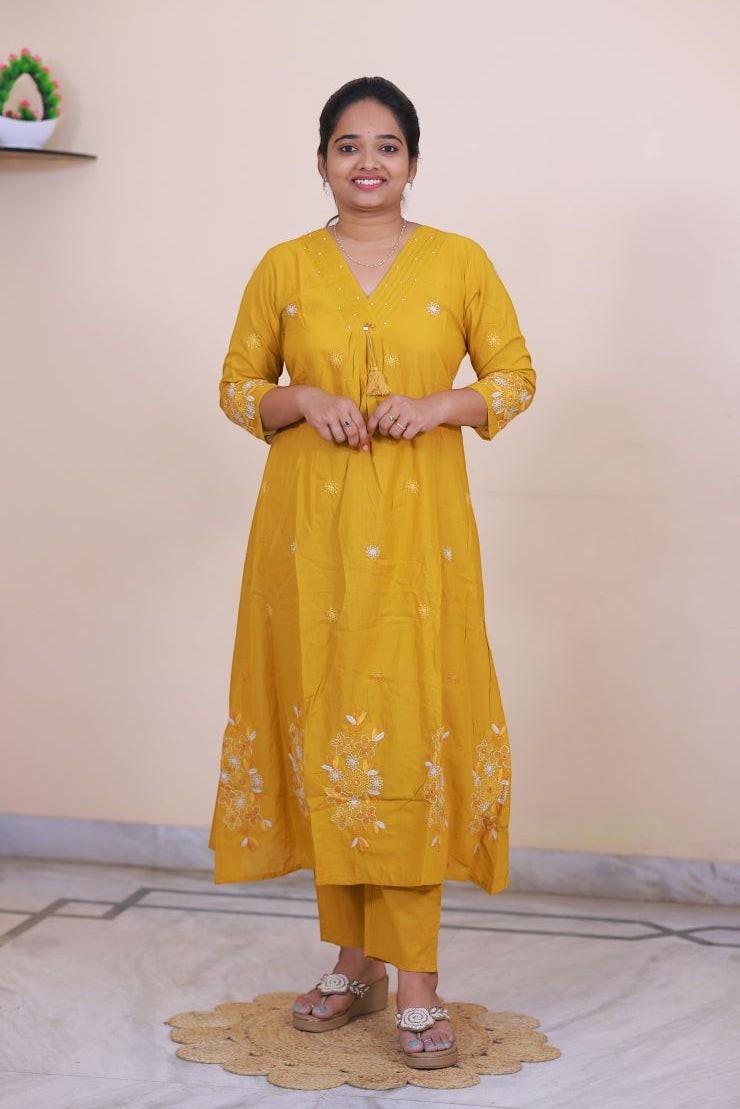 A woman wearing a mustard yellow SreeVastra cotton 3 piece dress with white floral embroidery and tassel detail.